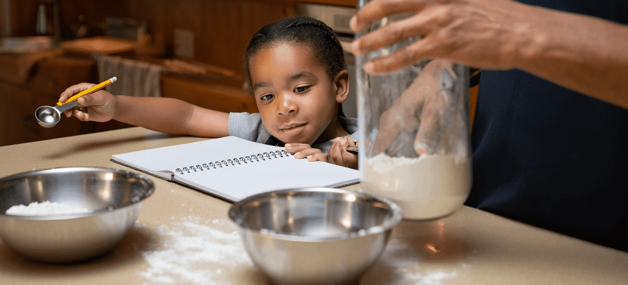 Child holding measuring spoon, adult's hand in flour jar, open notebook.